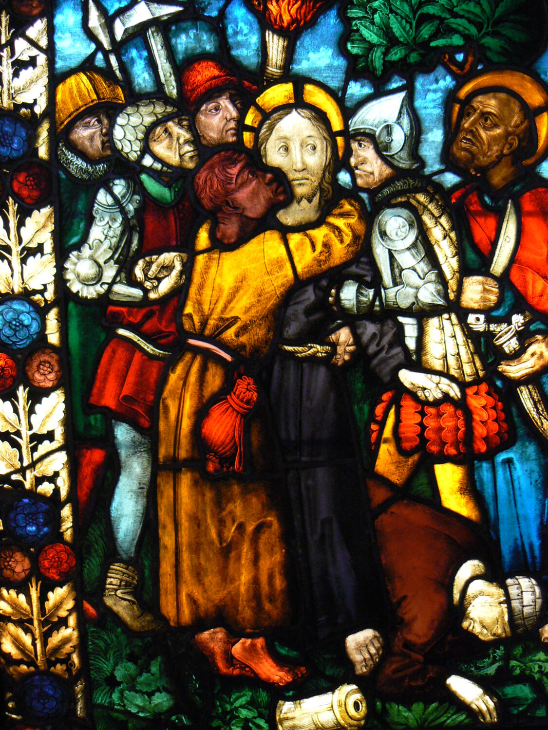 Un vitrail montrant Judas, accroché au cou de Jésus, donnant un baiser sur la joue du messie alors qu'il se fait arrêter par les autorités du Sanhedrin.