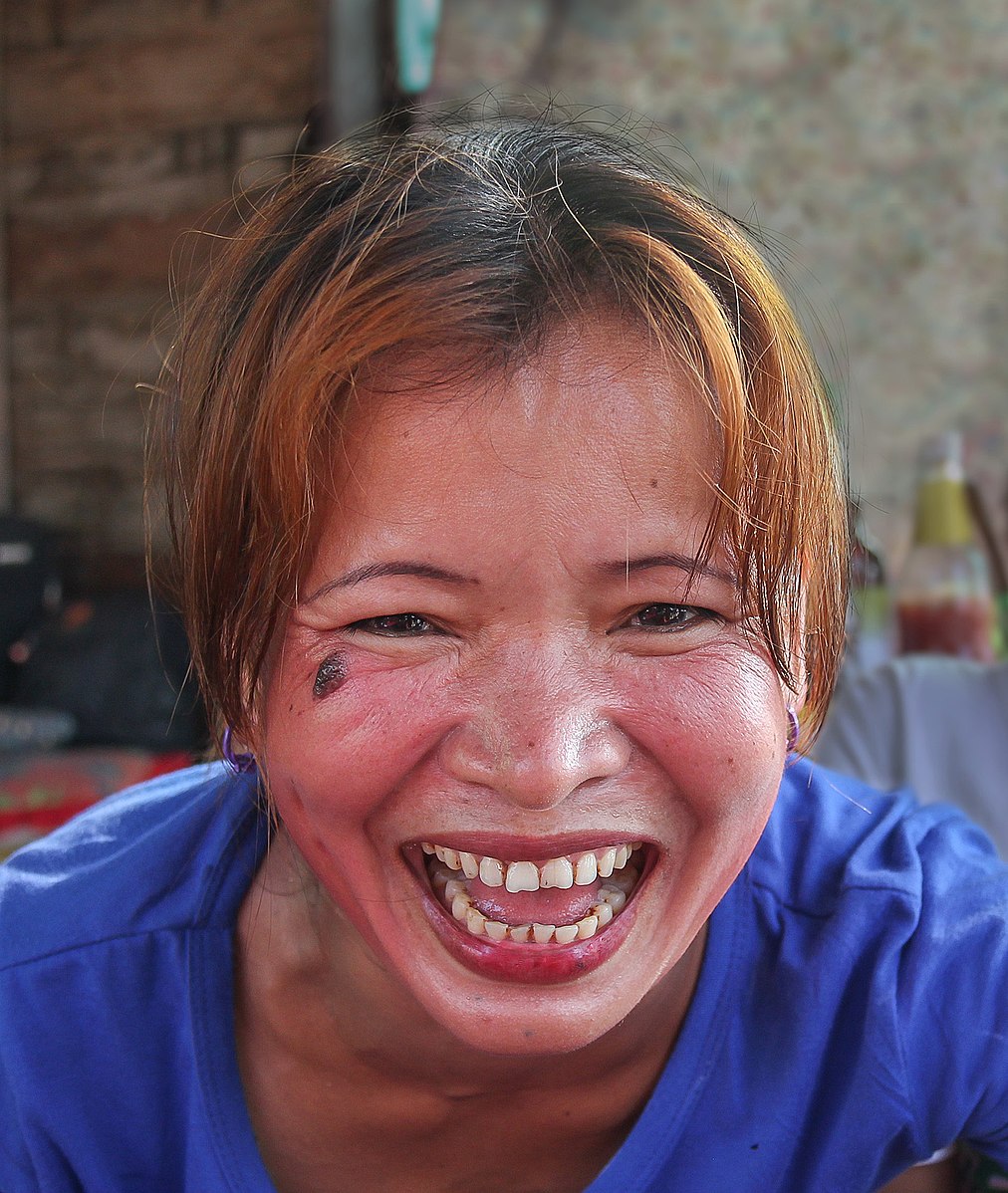 Une femme portant un t-shirt bleu foncé ri à gorge déployée en regardant droit devant elle.