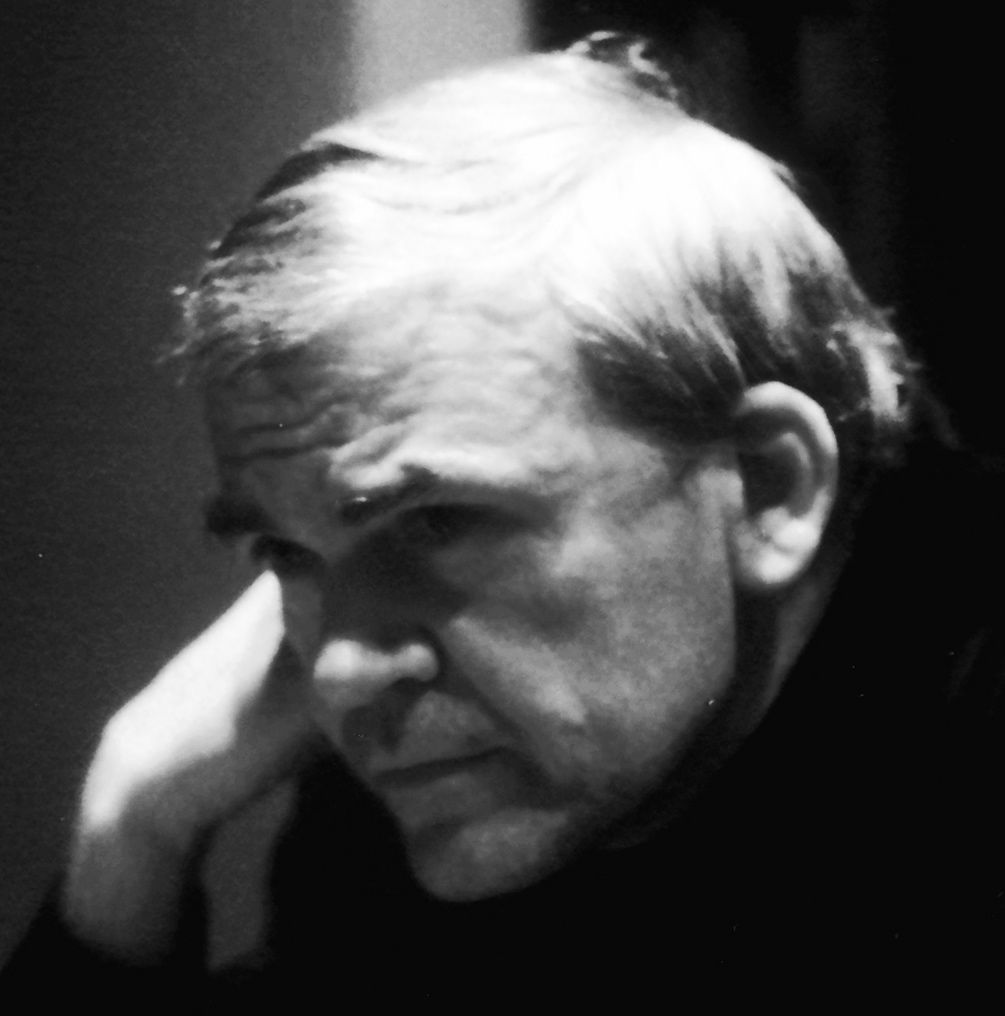 Kundera est photographié en noir et blanc. On voit son visage de profil. Il est accoté sur sa main droite, l'air penseur, et regarde hors-champ, le regard fixé sur la gauche.