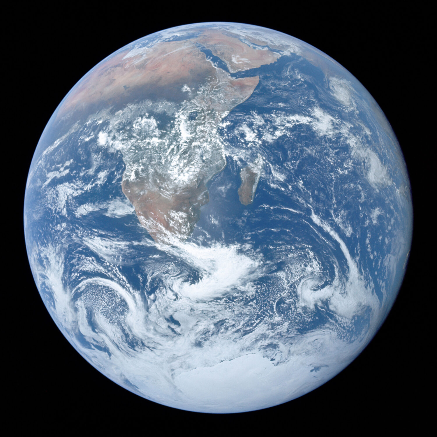 La photo nous montre la Terre prise de l'espace. Le globe est au milieu d'un carré noir. La photo montre l'Afrique, l'Antarctique et la péninsule arabique : les continents sont vus en brun-vert sous un couvert de nuages blancs, sauf l'Antartique qui couvre toute la portion sud du globe de blanc. Le cercle terrestre présente une majorité de bleu, les océans, eux aussi partiellement couverts de nuages blancs. 
