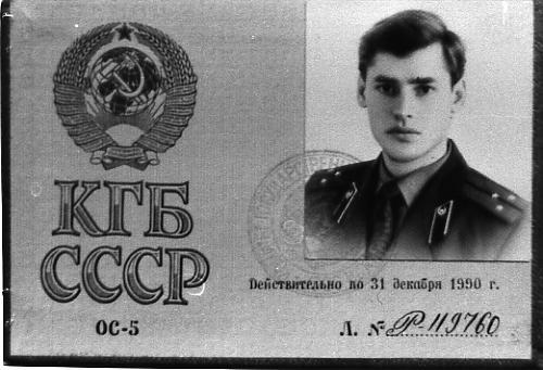 Une reproduction en noir et blanc d'une carte de membre du KGB. La carte d'identification rectangulaire montre une photo de l'agent dans le coin supérieur droit. Il s'agit d'un jeune homme en uniforme qui regarde droit dans l'appareil photo, l'air sérieux. Sous la photo, une ligne de texte en cyrillique et, sous ce texte, un numéro écrit à la main : P-119760. À gauche de la carte se trouve le logo du KGB, un espèce de globe avec le logo communiste entouré d'une couronne de blé. Sous ce logo, du texte cyrillique en gros caractères sur deux lignes. La supérieure montre ce qui semble se traduire par KGB et l'inférieure montre les lettre CCCP. 